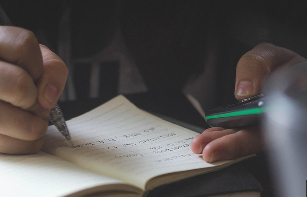 Student writes notes while looking at phone.